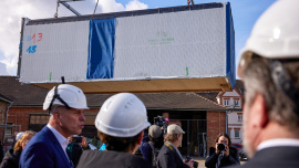 Bundesministerin Klara Geywitz auf dem Betriebsgelände von Timber Homes. Ein Wohnmodul schwebt am Kran hängend vor der Gruppe. Foto: Bojan Ritan / Bundesphoto